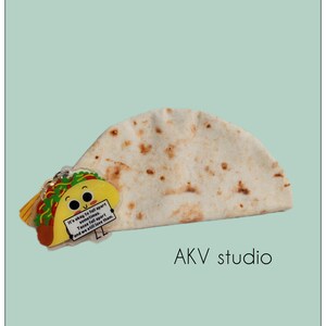 May include: A whimsical image featuring a tortilla and a taco-shaped keychain. The keychain has a smiling face and a sign that reads, "It's okay to fall apart sometimes. Tacos fall apart and we still love them." The background is a light teal color.