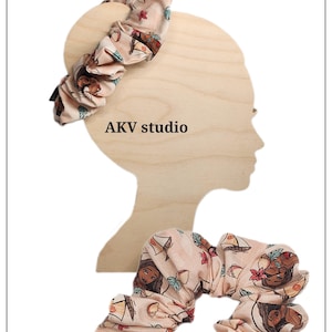 May include: Two scrunchies and a wooden silhouette. The scrunchies are patterned with a light pink background and illustrations of a woman, boats, and flowers. The wooden silhouette has the text "AKV studio".