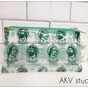May include: Clear plastic zippered pouch with a green and white print featuring the text "Cheech & Chong" and images of the two comedians. The text "Born in East LA" is repeated throughout the print.
