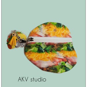 May include: A novelty coin purse and keychain set. The coin purse is shaped like a taco, featuring a zipper closure and a colorful print of taco ingredients. The keychain is a taco charm with a yellow tassel. The text "Tacos for some..." is visible.