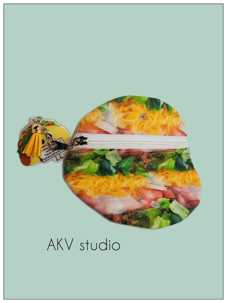 May include: A novelty coin purse and keychain set. The coin purse is shaped like a taco, featuring a zipper closure and a colorful print of taco ingredients. The keychain is a taco charm with a yellow tassel. The text "Tacos for some..." is visible.
