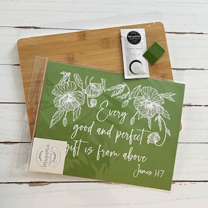 May include: A green stencil with white floral designs and the text "Every good and perfect gift is from above James 1:17" is displayed on a bamboo cutting board. A small packet of sample paste and a green applicator are also included.