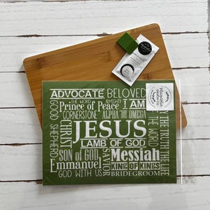 May include: A bamboo cutting board with a green card featuring the word "JESUS" and related terms in white. A small packet of "SAMPLE PASTE" and a green square are on the board.
