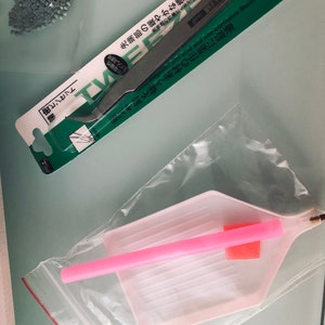 May include: A set of diamond painting tools including a pink tray with a pink applicator, and a pair of tweezers with a green and white label that reads "Non-magnetic anti-acid and non-corrosive Stainless Steel".