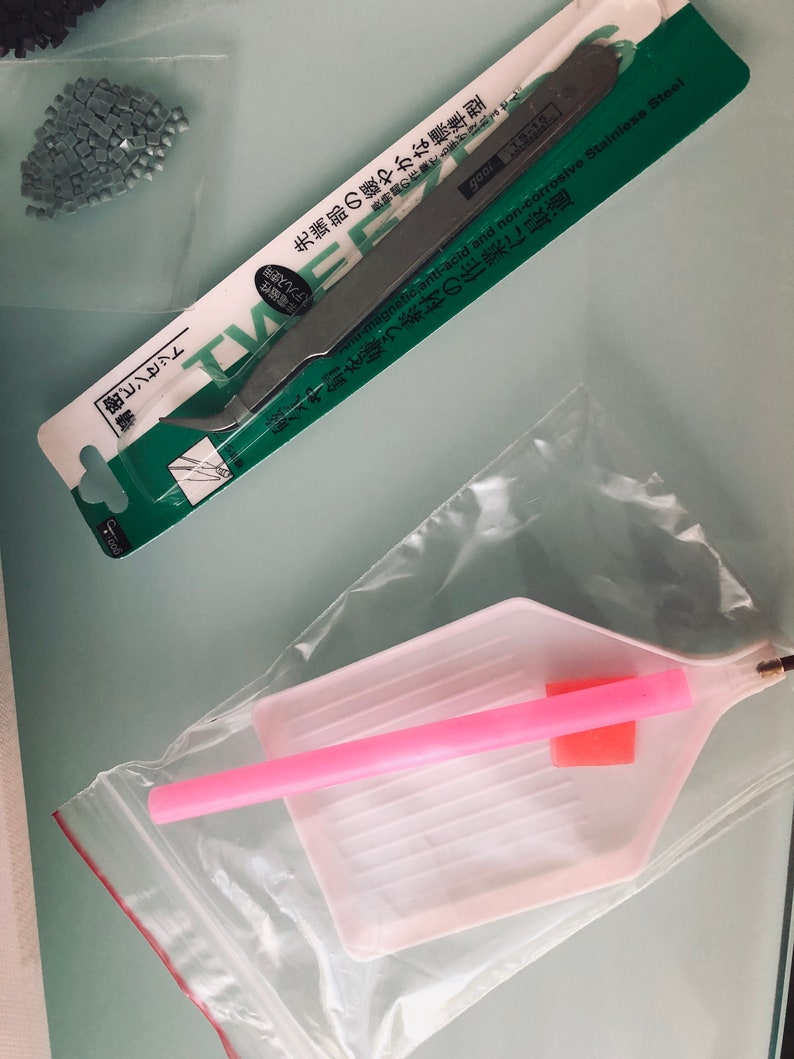 May include: A set of diamond painting tools including a pink tray with a pink applicator, and a pair of tweezers with a green and white label that reads "Non-magnetic anti-acid and non-corrosive Stainless Steel".