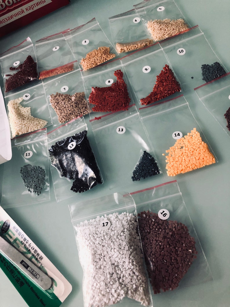 May include: Assortment of small plastic bags containing various colors of tiny square beads, labeled with numbers 1 through 17. The bags are arranged in rows on a white surface.