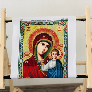 Op de afbeelding: Een houten borduurstandaard met een wit canvas waarop een diamant schilderij van de Maagd Maria en baby Jezus is afgebeeld. Het canvas is getiteld "Образ Пресвятой Богородицы "Казанская" en "ДАЛ-0-318".