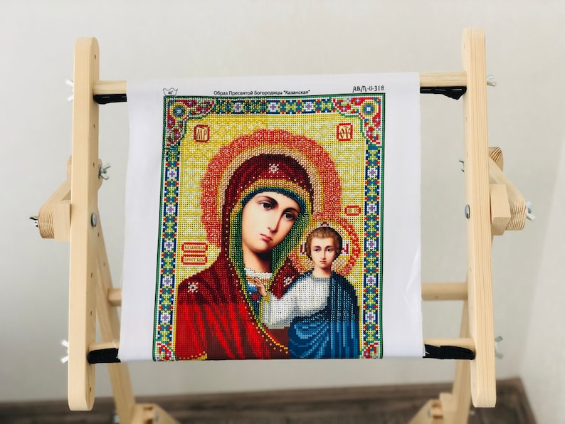 Op de afbeelding: Een houten borduurstandaard met een wit canvas waarop een diamant schilderij van de Maagd Maria en baby Jezus is afgebeeld. Het canvas is getiteld "Образ Пресвятой Богородицы "Казанская" en "ДАЛ-0-318".