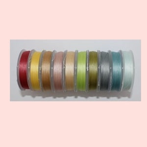 May include: Ten spools of thread in various colors, including red, yellow, brown, pink, green, gray, and blue. The spools are arranged in a row and are all in clear plastic containers.