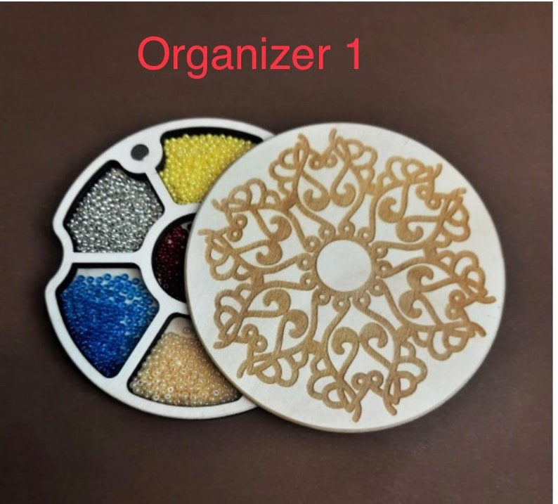 May include: A wooden organizer with six compartments, each filled with different colored beads. The organizer has a lid with a decorative design.