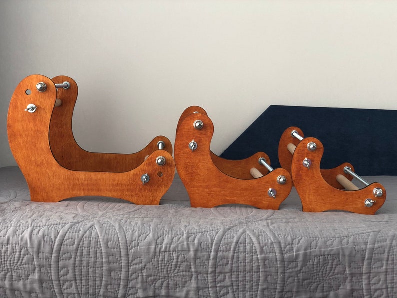 May include: Three wooden yarn winding stands of different sizes. The stands are made of stained wood and have metal hardware. The stands are arranged in order of size, with the largest stand on the left and the smallest stand on the right.