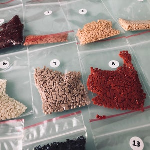 May include: Close-up of 10 small plastic bags filled with various colored diamond-shaped beads. The bags are labeled with numbers 1 through 9 and 13.