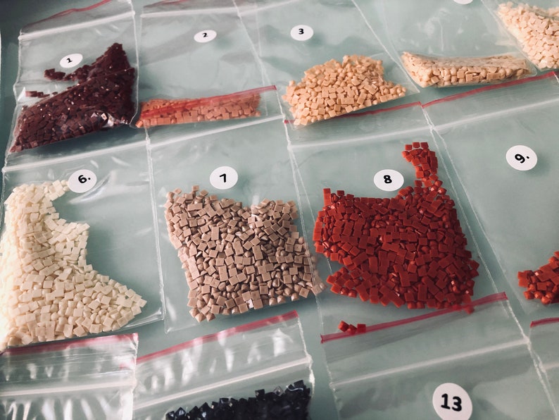 May include: Close-up of 10 small plastic bags filled with various colored diamond-shaped beads. The bags are labeled with numbers 1 through 9 and 13.