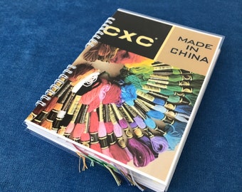 May include: A spiral-bound CXC embroidery floss color chart. The cover features the CXC logo and the text "MADE IN CHINA". The chart displays a wide array of colorful embroidery floss, with strands of floss extending from the pages.