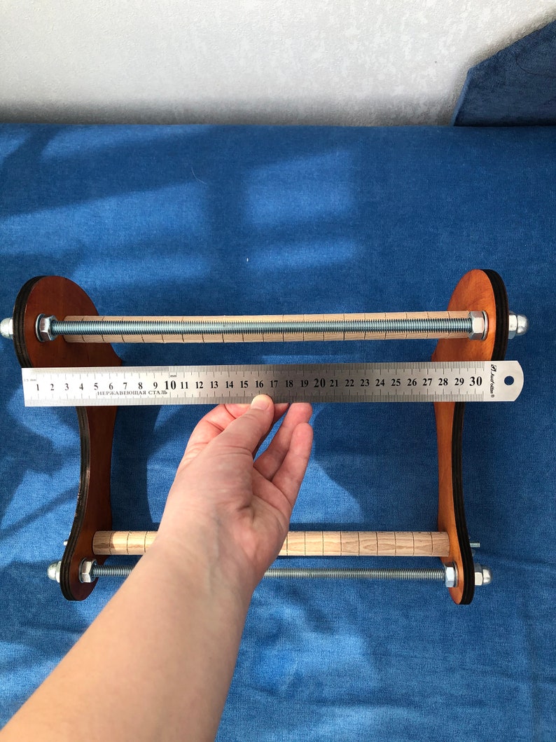 May include: A wooden loom with two metal rods and a ruler measuring 30 inches. The loom is brown with a black base and has a metal screw on each side.