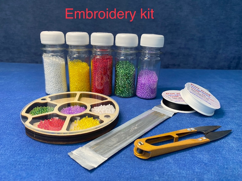 May include: Embroidery kit with six small bottles of colorful beads, a wooden bead organizer, a spool of black thread, a spool of white thread, a package of needles, and a pair of small scissors.