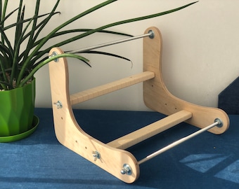 May include: A wooden loom with two metal rods and a wooden frame. The loom is made of light wood and has a natural finish.
