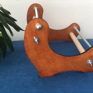 May include: A wooden loom with two metal rods and adjustable tension knobs. The loom is stained a light brown color and has a curved base.