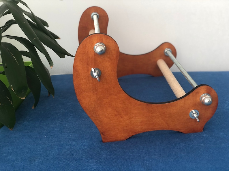 May include: A wooden loom with two metal rods and adjustable tension knobs. The loom is stained a light brown color and has a curved base.
