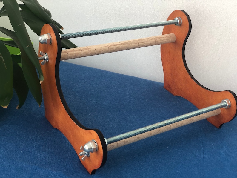 May include: Wooden loom stand with two wooden dowels and metal rods. The stand is stained a light brown color and has a black border.
