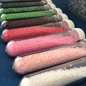 May include: A set of ten clear glass tubes filled with various colors of seed beads. The beads are arranged in order of color, starting with dark brown and ending with white.