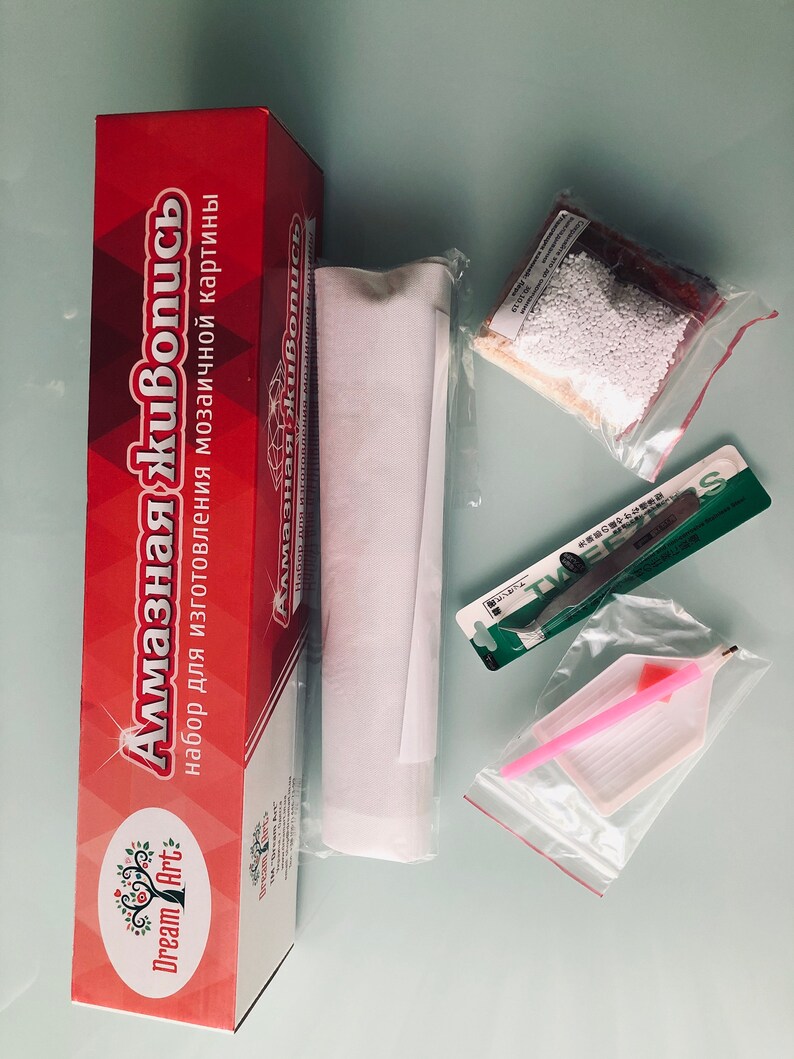 May include: A red box with the text "Алмазная живопись" and "Dream Art" on it. The box contains a white canvas, a bag of white beads, a pink tool, a green tool, and a clear plastic bag with a pink tool.