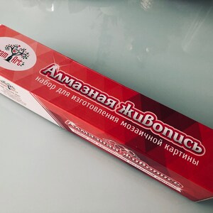 May include: A red box with the text "Алмазная живопись" and "набор для изготовления мозаичной картины" in white. The box is labeled "Dream Art" with a logo of a tree with a red apple.