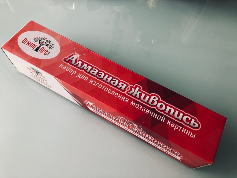May include: A red box with the text "Алмазная живопись" and "набор для изготовления мозаичной картины" in white. The box is labeled "Dream Art" with a logo of a tree with a red apple.
