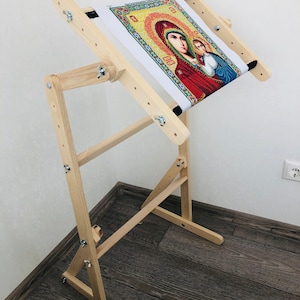 Könnte beinhalten: Ein hölzerner Stickrahmen mit einem darüber gespannten Stoff. Der Stoff zeigt ein farbenfrohes Bild einer religiösen Ikone. Der Rahmen hat verstellbare Beine und einen integrierten Rahmen.