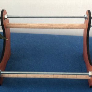 May include: A wooden yarn winder with two wooden dowels and metal tension rods. The winder is brown with black accents.
