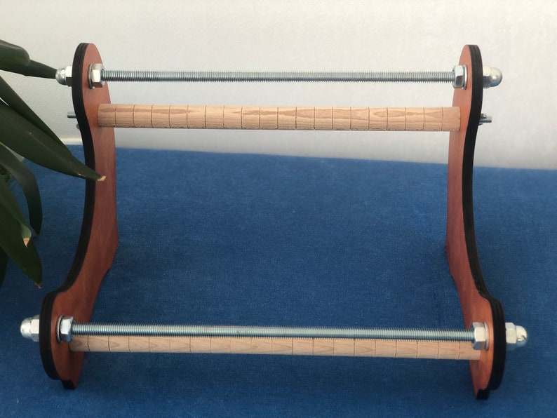 May include: A wooden yarn winder with two wooden dowels and metal tension rods. The winder is brown with black accents.