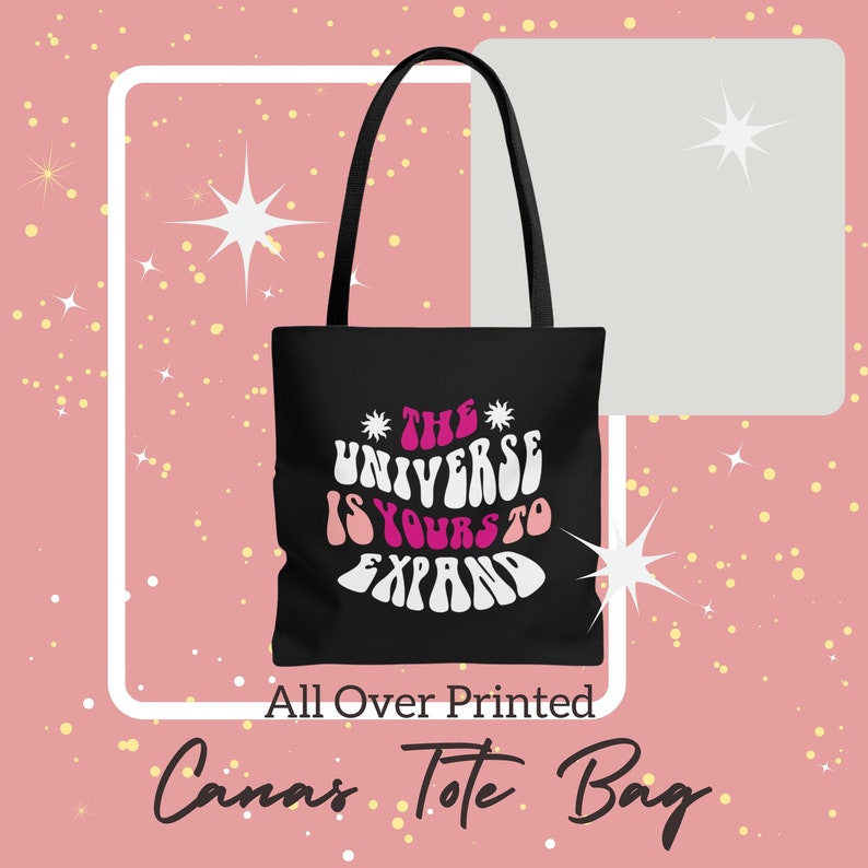 May include: Black canvas tote bag with white text that reads "The Universe Is Yours To Expand" in a retro font. The text is outlined in pink.