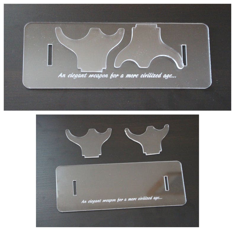 May include: Clear acrylic display stand with two curved supports and a rectangular base. The text "An elegant weapon for a more civilized age..." is etched on the base. The stand is designed to hold a specific item.
