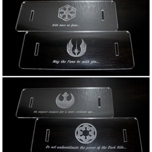 May include: Four clear acrylic plaques with engraved designs and text. The top plaque features a symbol and the text "Sith have no fear...". The second plaque has a symbol and the text "May the Force be with you...". The third plaque has a symbol and the text "An elegant weapon for a more civilized age...". The fourth plaque has a symbol and the text "Do not underestimate the power of the Dark Side..."