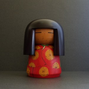 May include: A wooden doll with black hair, closed eyes, and a red and yellow floral dress.