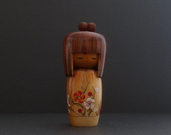 May include: A wooden Japanese kokeshi doll with brown hair, closed eyes, and a painted floral pattern on its dress.