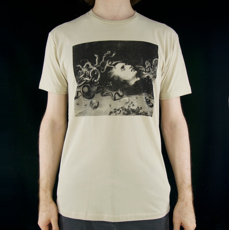 K&ouml;nnte beinhalten: Ein beiges T-Shirt mit einem Schwarzwei&szlig;bild von Medusa, einer mythischen griechischen Kreatur mit Schlangenhaaren, auf der Vorderseite.