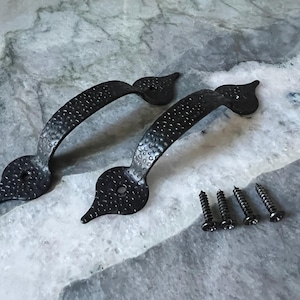 May include: Two black, hammered-finish cabinet handles with decorative ends and matching screws. The handles have a curved design and a textured surface, perfect for adding a rustic touch to furniture or cabinetry.