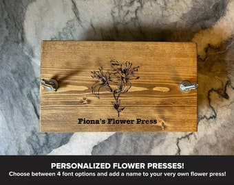 May include: A wooden flower press with two metal clamps. The press is personalized with the text "Fiona's Flower Press".