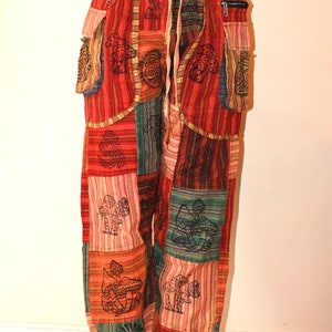 May include: Patchwork trousers with a red, orange, green and blue striped pattern. The trousers have a drawstring waist and side pockets. The fabric is printed with mushrooms and other designs.
