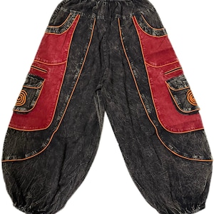 Peut inclure: Pantalon de style harem noir et rouge avec une taille élastique. Le pantalon présente des panneaux rouges avec des poches et des coutures orange. Le design comprend un motif en spirale sur les poches. Coupe ample et décontractée.