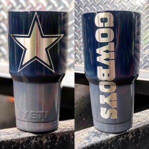 May include: A dark blue and gray Yeti tumbler with a silver star and the word "COWBOYS" in silver lettering.