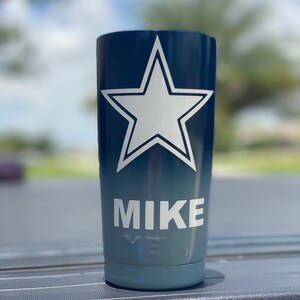 May include: A blue and gray tumbler with a white star and the name "MIKE" printed on it.