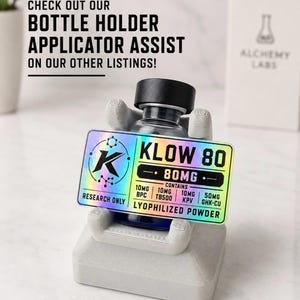May include: A small glass vial with a black cap sits in a light gray 3D-printed stand. A rectangular holographic label on the vial reads KLOW 80, 80MG, RESEARCH ONLY, LYOPHILIZED POWDER, and lists 10MG BPC, 10MG TB500, 10MG KPV, and 50MG GHK-CU.