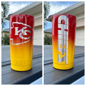 May include: Two stainless steel tumblers with a red and yellow ombre design. One tumbler has the Kansas City Chiefs logo and the other says "Chiefs". Both tumblers have the Yeti logo on the bottom.