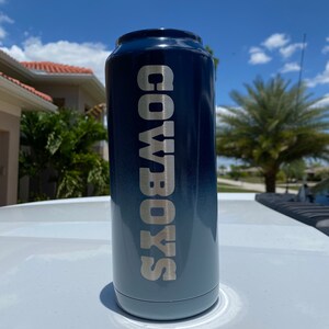 May include: A blue and black can cooler with the text "COWBOYS" in silver lettering.