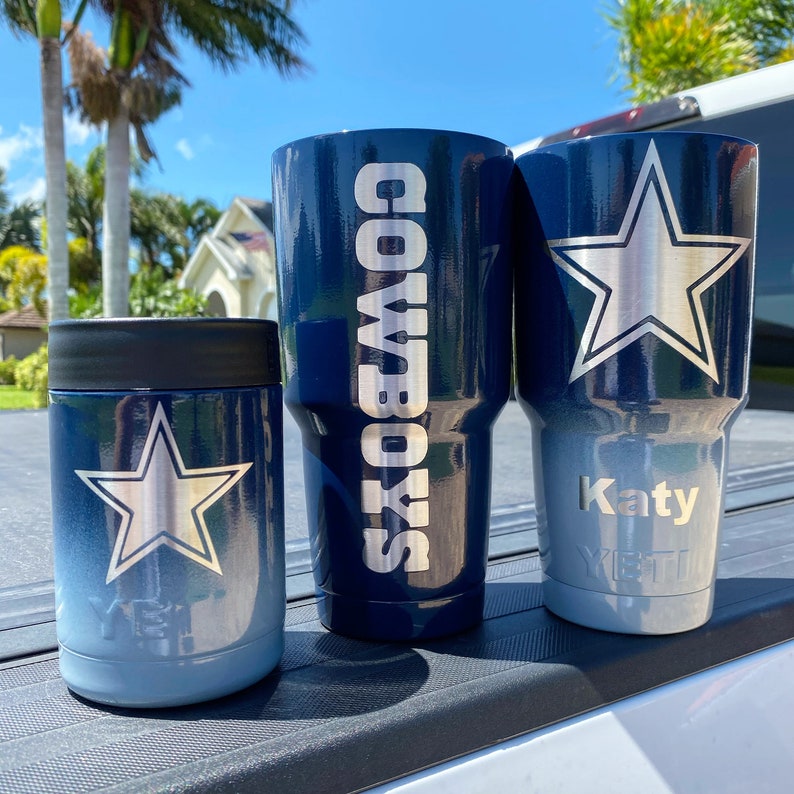 May include: Three stainless steel tumblers with a blue and silver ombre finish. The tumblers feature a silver star and the words "Cowboys" and "Katy".