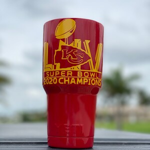 May include: Red Yeti tumbler with a gold Super Bowl LV logo and the text "2020 Champions".