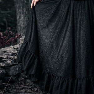 A black skirt with a floral pattern and a ruffled hem. The skirt is made of a soft lace fabric.