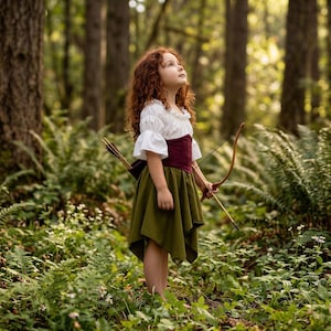 May include: A young person in a forest setting, wearing a white blouse with ruffled sleeves, a burgundy corset, and an olive green skirt. They are holding a bow and arrow, with a quiver of arrows on their back. The outfit has a medieval or fantasy theme.